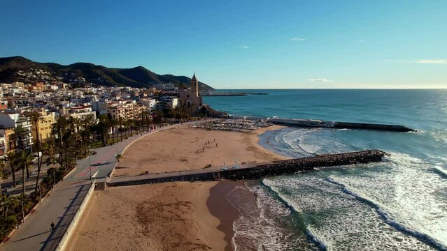Panoramic aerial drone view of coastal village, Sant Bartomeu i Santa Tecla de Sitges during sunny day in Sitges, town near Barcelona in Catalonia, Spain. It is famous for its beaches and nightlife