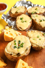 Wooden board with tasty baked potato and cheese, closeup