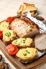 Wooden board with tasty baked meat, potatoes and tomatoes on table, closeup