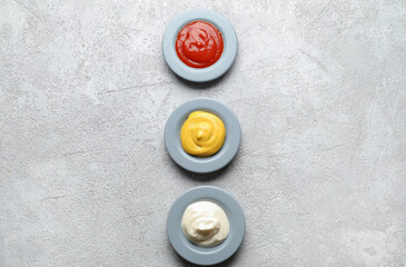 Plates with ketchup, mayonnaise and mustard on grey grunge table