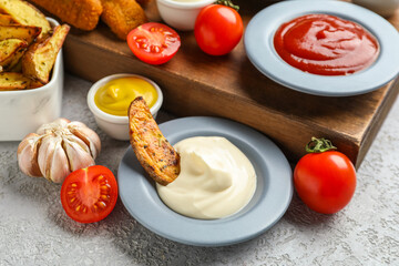Composition with different sauces and dipped potato wedge on grey grunge table