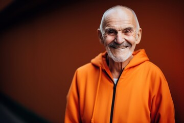 Obraz premium smiling senior man in orange hoodie looking at camera isolated on orange