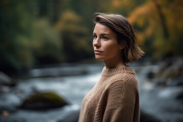Portrait of a beautiful young woman in a beige sweater on the background of a mountain river.