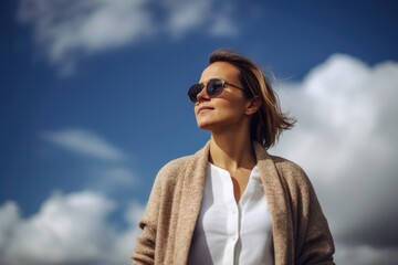 Portrait of young beautiful woman in sunglasses against blue sky with clouds
