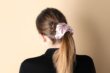 Woman with ponytail and silk scrunchy on beige background, back view