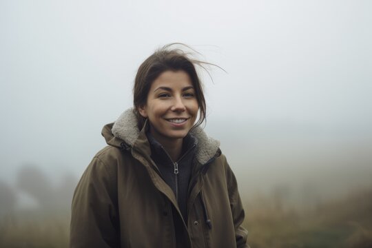 young beautiful hipster woman in hat and jacket walking in foggy field on cold autumn day