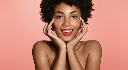 Gorgeous African American woman applies eye patches for better blood flaw, natural clear skin tone...