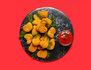 Slate board of tasty nuggets with ketchup on red background