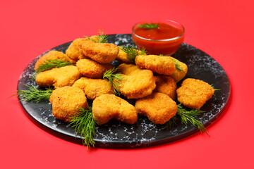 Slate board of tasty nuggets with ketchup on red background