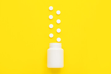 Bottle with white pills on yellow background
