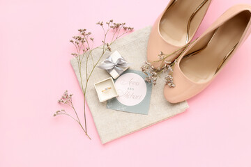 Box with engagement ring, flowers, heels and wedding invitation on pink background