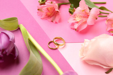 Wedding rings with flowers on color background, closeup