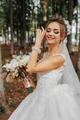 A beautiful young woman in a wedding dress between tall trees in the forest with a royal hairstyle...