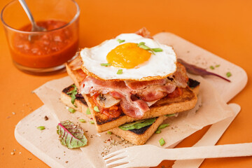 Delicious sandwich with fried egg and bacon on orange background