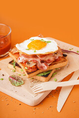 Delicious sandwich with fried egg and bacon on orange background