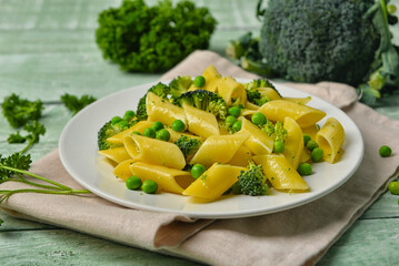 Plate with tasty penne pasta and broccoli on green wooden  background