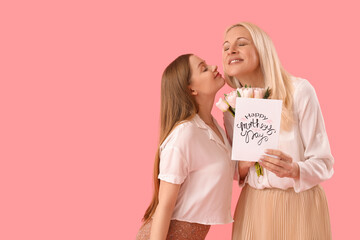 Young woman greeting her mother with tulips and card on pink background
