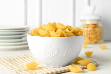 Bowl with raw conchiglie pasta on light background