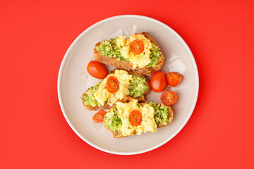 Plate with tasty scrambled eggs sandwiches and vegetables on red background