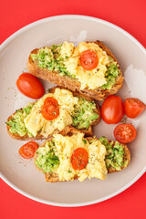 Plate with tasty scrambled eggs sandwiches and vegetables on red background