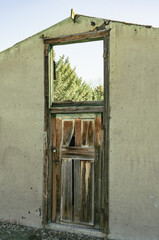 Old abandoned building is missing a roof, a top window, and other walls. It is open to the sky and the door below is worn out but has a lock to keep it secure. 