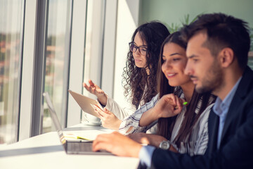 Creative business team sharing laptop in office, watching startup presentation, brainstorming, pointing at monitor, talking.