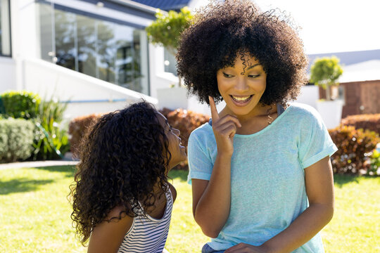 Smiling biracial mother asking for a kiss from her daughter in garden on sunny day
