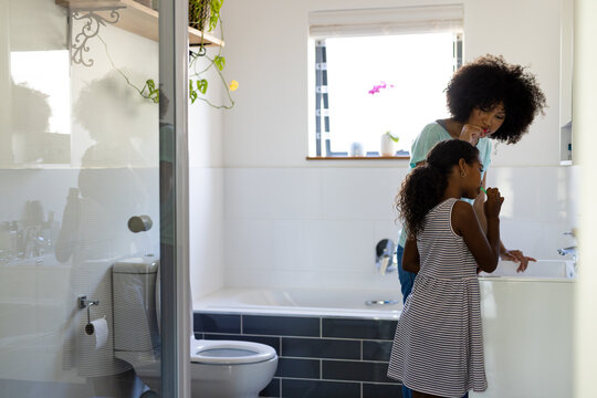 Happy biracial mother and daughter brushing teeth together in bathroom