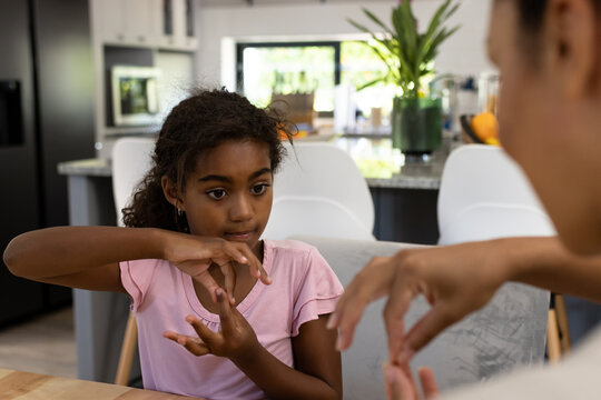 Focused biracial mother sitting at table teaching her daughter sign language