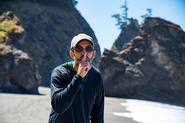 Adventurous athletic man motioning to be quiet on a beach on the rugged coastline of the Pacific Northwest.
