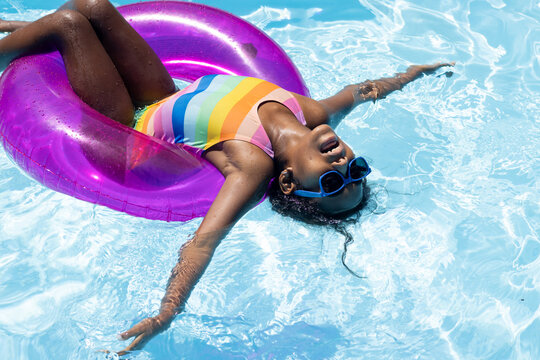 Happy biracial girl with sunglasses relaxing on inflatable in swimming pool