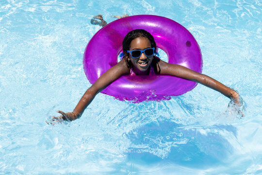 Portrait of happy biracial girl with sunglasses playing with inflatable in swimming pool