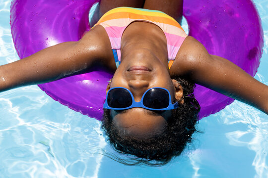 Portrait of happy biracial girl with sunglasses relaxing on inflatable in swimming pool