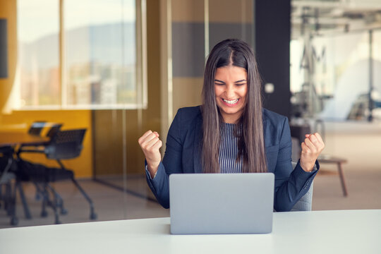 Young brunette woman working at the office with laptop success sign doing positive gesture with hand, thumbs up smiling and happy.
