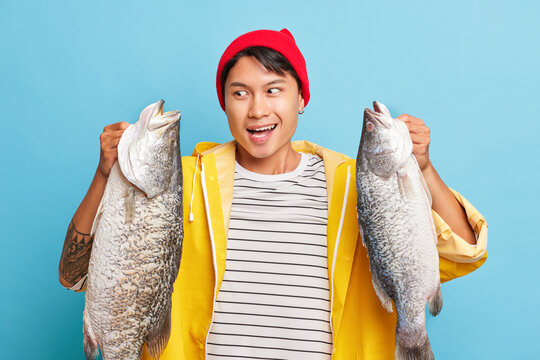 Young happy man holds two huge fish in his hands, cute smiling guy posing in the studio, cheerfully looking at his catch, fishing time concept, copy space, high quality photo