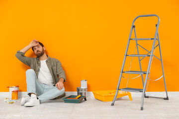 Tired designer sitting on floor near freshly painted orange wall indoors