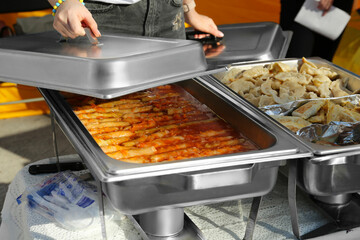 Female volunteer distributing delicious stuffed cabbage, dumplings and patties from food warmers