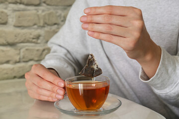 Woman taking tea bag out of cup at table indoors, closeup