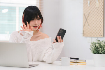 In a cozy living room at home, a beautiful young woman engrossed in messaging on her smartphone...