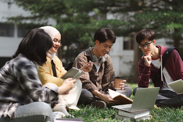 A multiethnic group of asian university students is seen studying together while sitting on the grass near the campus.