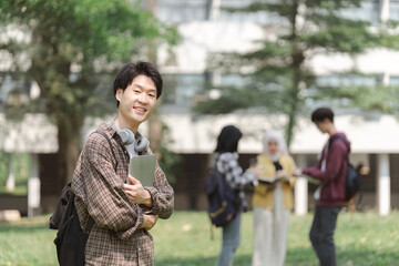 A portrait of a young Asian university student standing outside a building with his friends in the background.