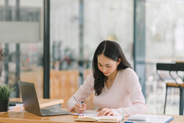 A portrait of a smiling, young, beautiful, professional, and confident millennial Asian businesswoman using a digital tablet to analyze sales data at a co-working space.