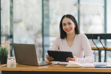 A portrait of a smiling, young, beautiful, professional, and confident millennial Asian businesswoman using a digital tablet to analyze sales data at a co-working space.