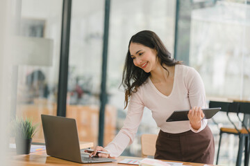 A portrait of a smiling, young, beautiful, professional, and confident millennial Asian businesswoman using a digital tablet to analyze sales data at a co-working space.