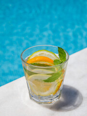 Citrus and mint leaves infused water, cocktail, lemonade in glass near pool. Summer iced cold drink