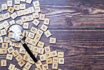 Fototapeta na wymiar English alphabet made of square wooden tiles with the English alphabet scattered on table background. The concept of thinking development, grammar. Magnifier placed on English letters