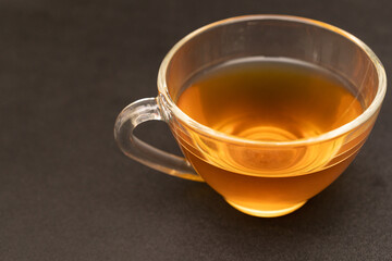 Glass cup of hot ginger tea on the black desk.