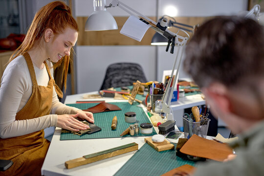 pleasant ginger woman with ponytail in orange apron oils wallet, purse, close up photo. blurred foreground