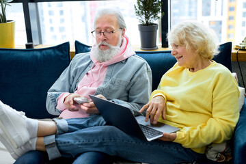 Happy mature retired couple using laptop and smartphone, reading news or watching tv series online. aged caucasian people communicating in social network, old people and modern tech concept