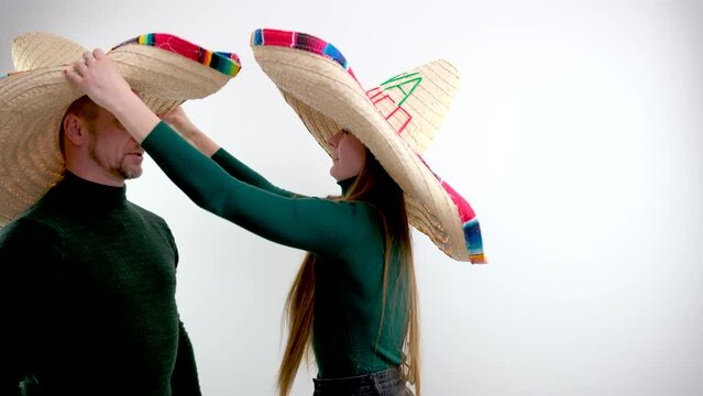 a girl puts a sombrero hat on a man a huge hat with large brim Green clothes on a white background fooling around a man turns his hat like an emperor